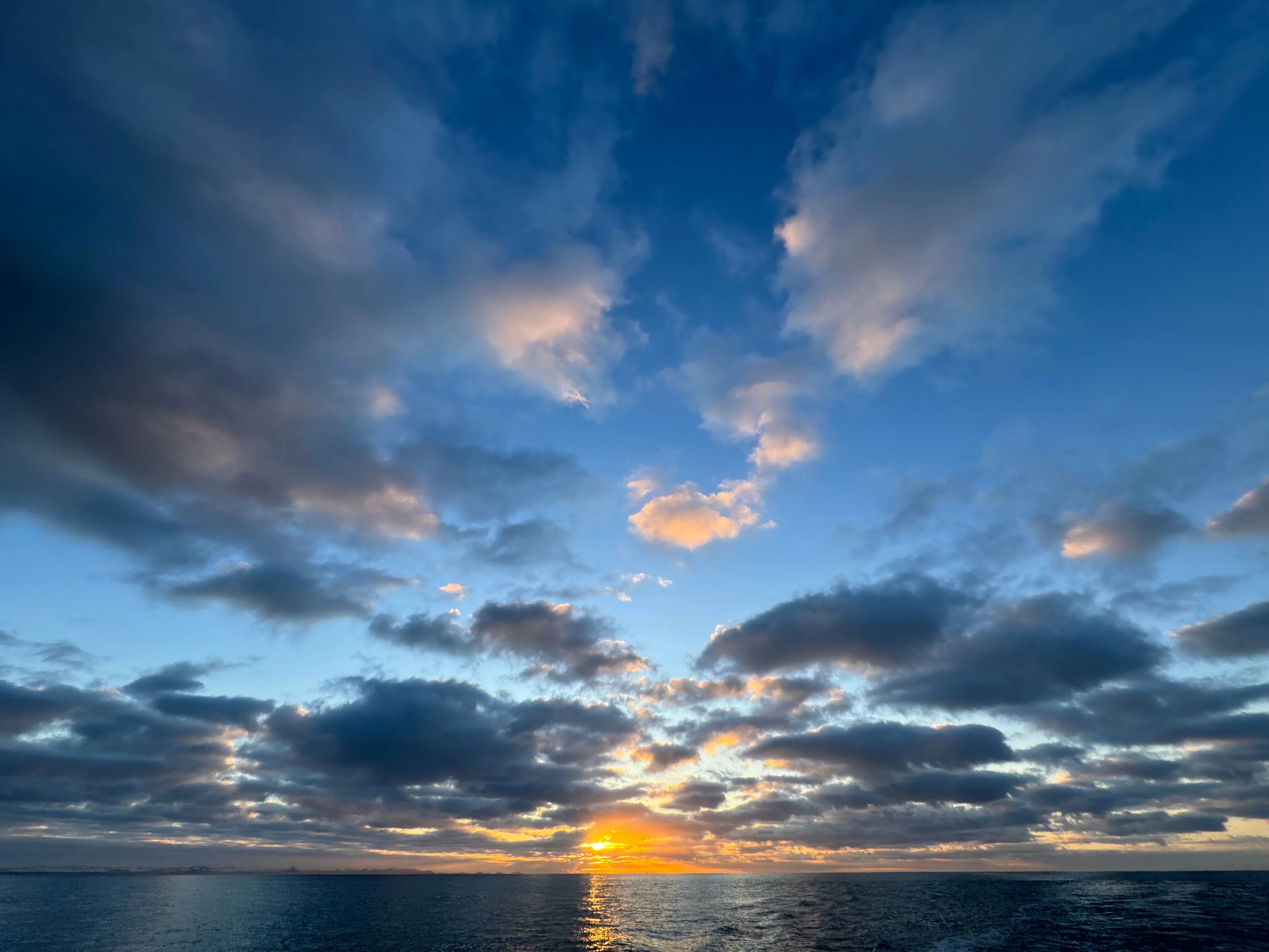 A wide field of scattered cloud over open sea, lit gold along the horizon by a low sun.